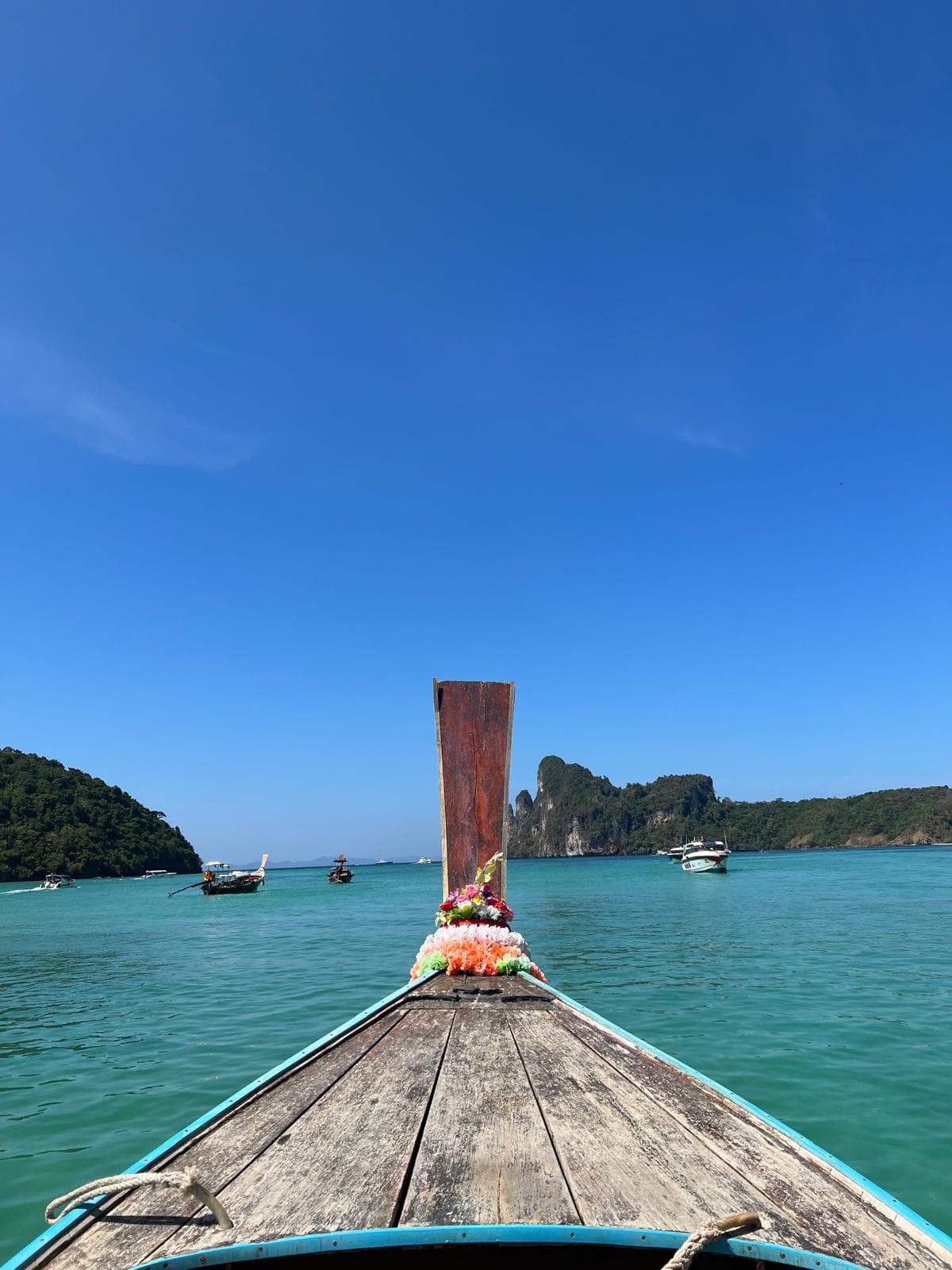 The decorated bow of a wooden boat facing turquoise water and distant cliffs
