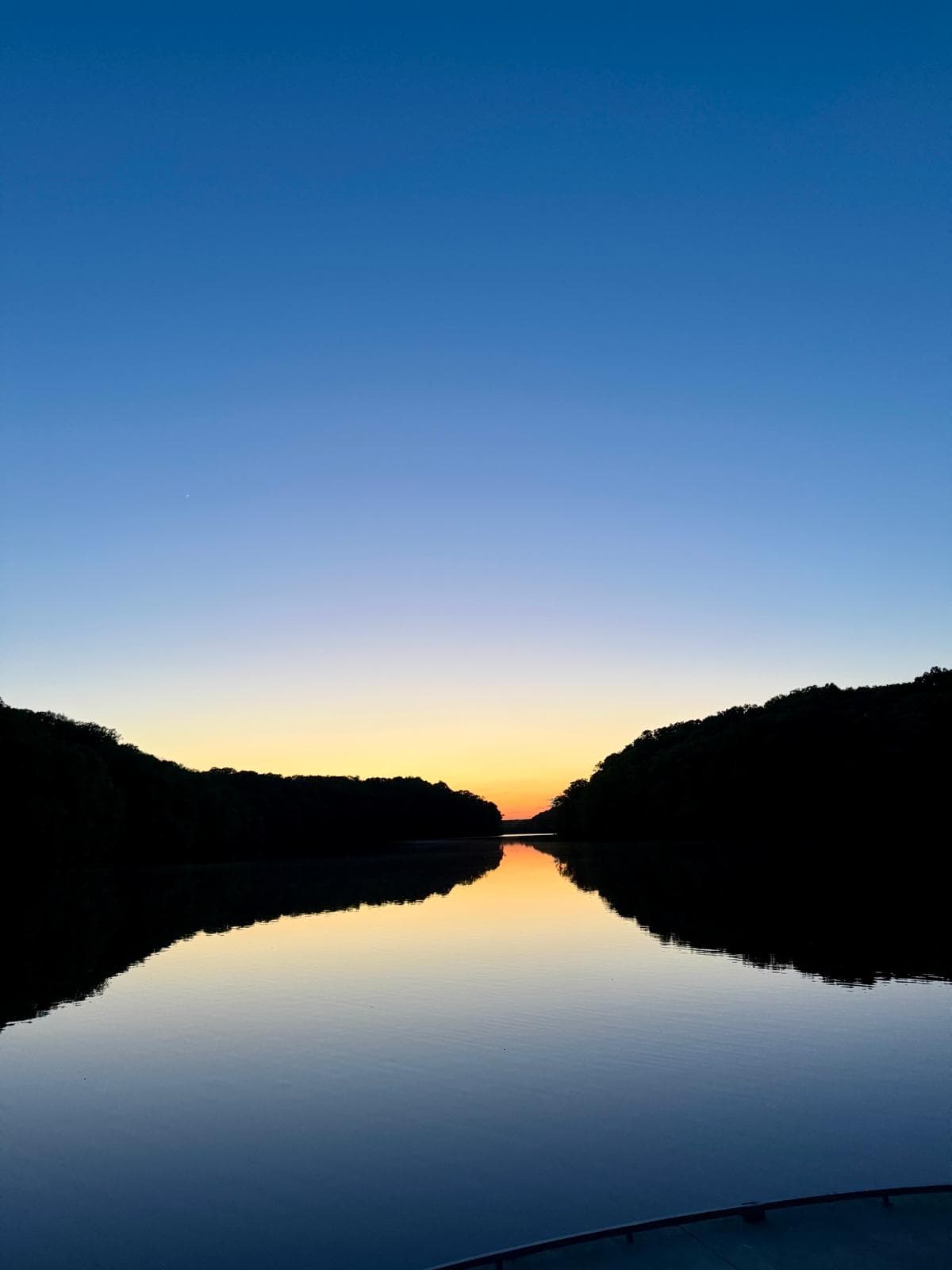 The last light of sunset reflected in still water between wooded banks